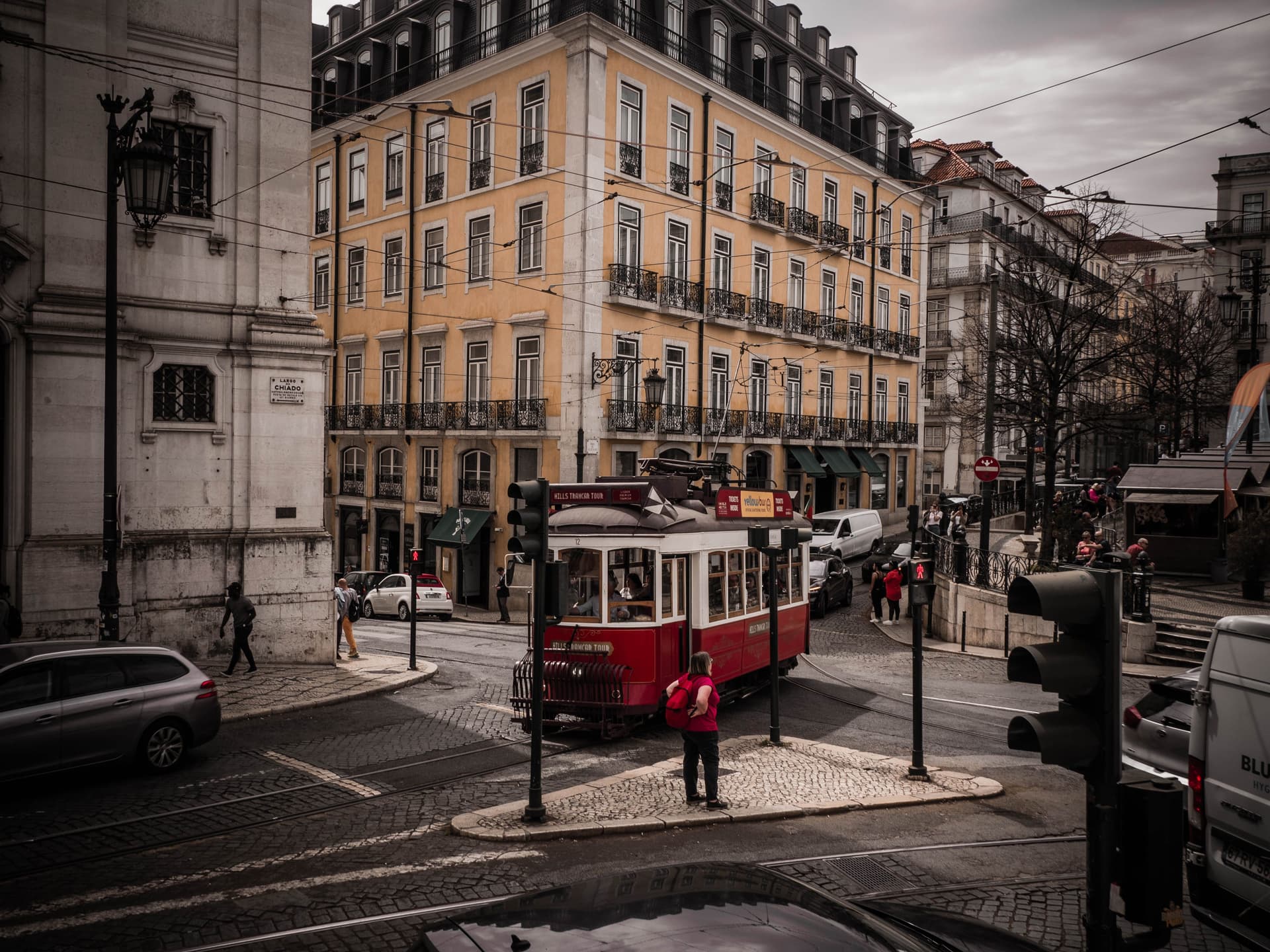 Red vintage tram travels through a cobblestone intersection lined with historic buildings in Lisbon, Portugal