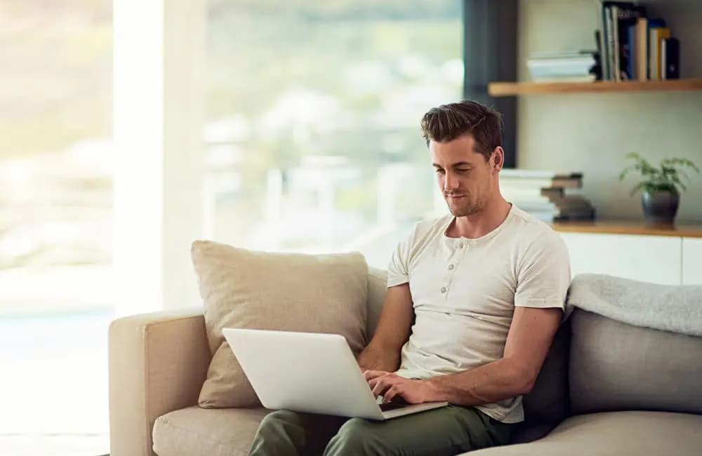 Man sitting on couch using laptop – workations trend. Image: Shutterstock